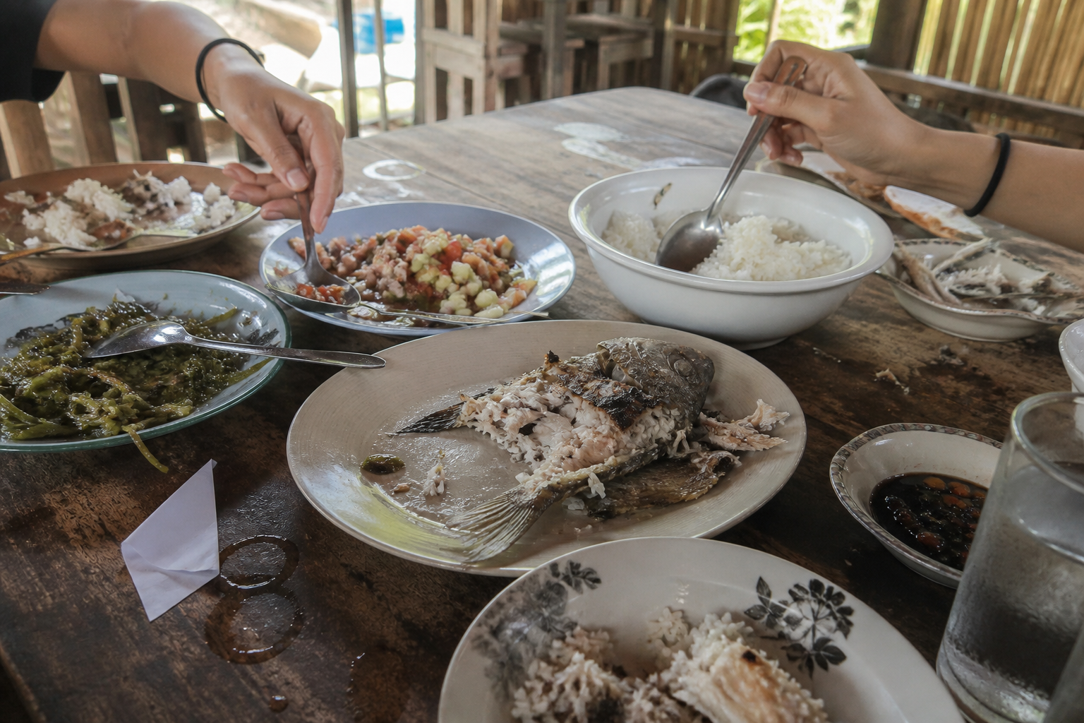 A shared table of grilled fish, rice, seaweed, tomato salad and a dipping sauce