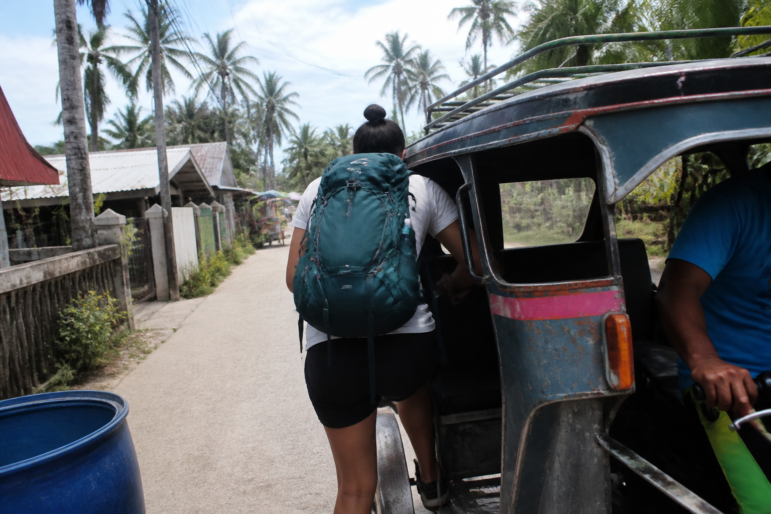 A backpacker boarding a well-used local tricycle on a village road