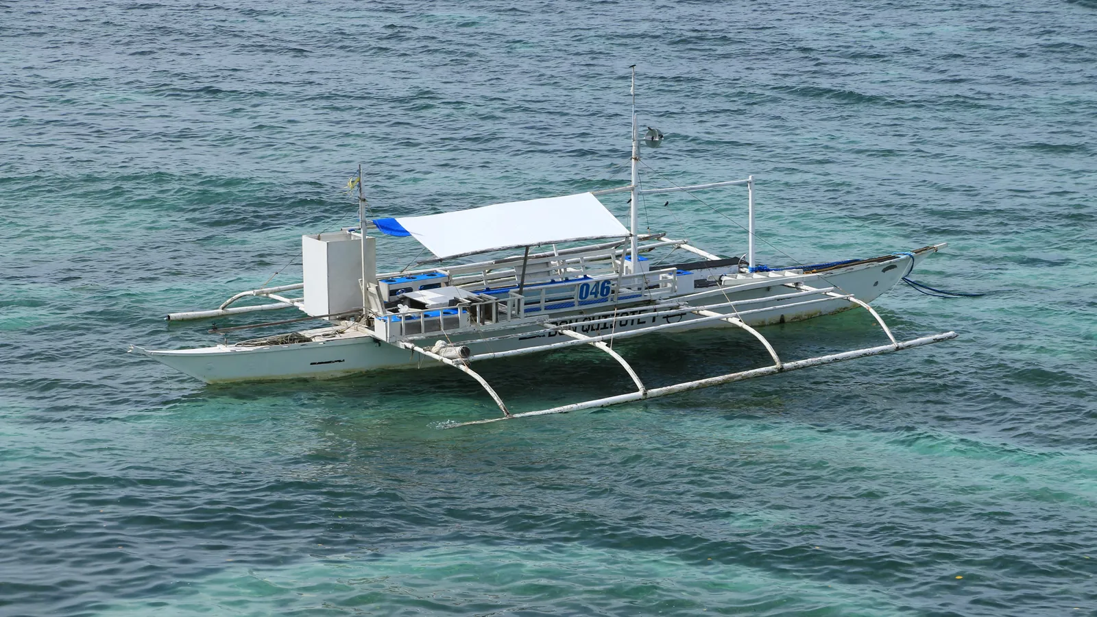 A white outrigger bangka with a canvas canopy floating on clear turquoise water